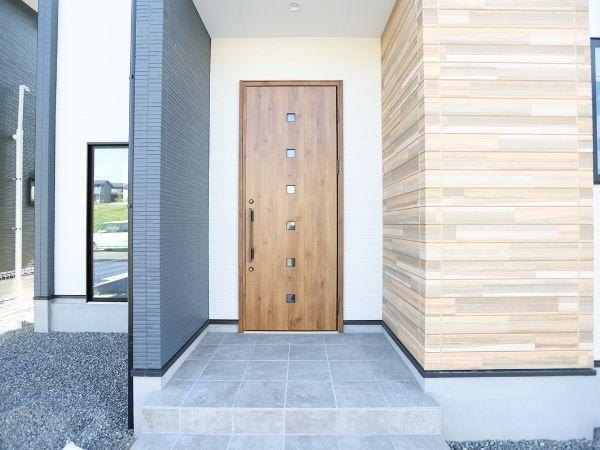 挾間町下市2期9号棟の玄関|木目調のドアが印象的な玄関です。タイル張りのアプローチが清潔感を演出しています。外観のモダンなデザインが目を引きます。シンプルな空間が引き立つ玄関です。重厚感のある仕上がりとなっています。