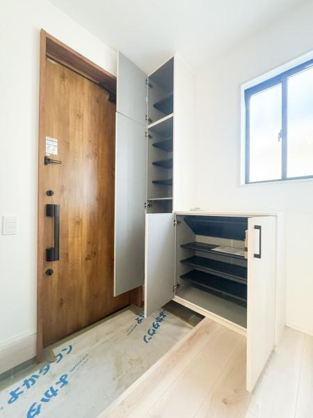 羽屋4丁目1期1号棟の玄関|木目調の扉がアクセントとなった玄関です。大きなシューズボックスが備え付けられており収納力に優れています。窓から光が差し込むため玄関スペースが明るい印象です。