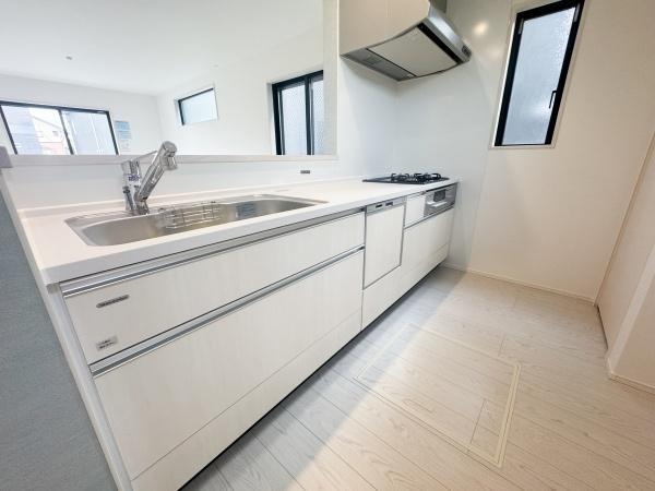 大字森町3期1号棟のキッチン|明るい室内に調和したキッチンは清潔感のある色合いが印象的です。作業スペースが広く換気もしやすい設計です。窓が複数あり自然光が差し込みます。シンプルで機能的な空間です。