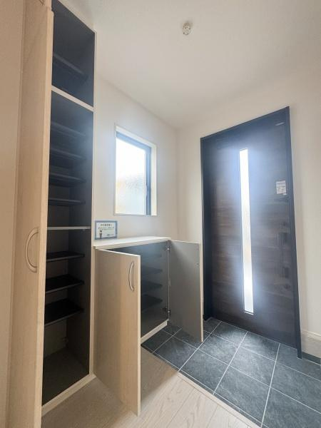 大字森町3期1号棟の玄関|明るい玄関スペースが印象的です。収納も豊富で整理整頓がしやすい作りになっています。窓から自然光が差し込み清潔感があります。落ち着いた色合いの床と扉が調和しています。出入りがしやすい広さも魅力です。