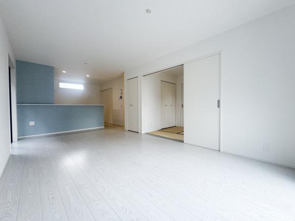 大字森町3期1号棟の居間・リビング|明るく開放感のあるリビングです。白を基調とした床と壁が空間を広く感じさせます。隣接する和室との一体感も特徴です。キッチンカウンターがアクセントになっています。収納が充実している点もポイントです。