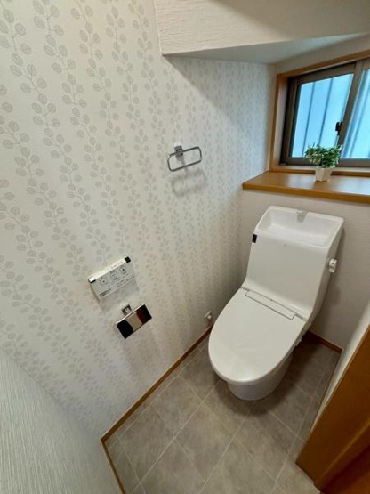 【トイレ】 | 清潔感のあるトイレ空間です。すっきりとしたデザインで明るい雰囲気が魅力です。窓から自然光が入り換気も快適に行えます。壁紙のデザインがアクセントになっています。収納スペースも確保されています。