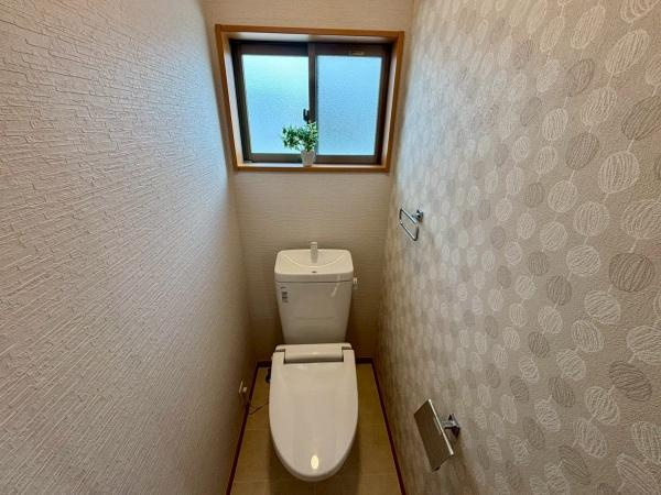 【トイレ】 | 明るい採光が入る窓付きで空間が開放的に感じられます。壁紙のデザインが落ち着いた印象を演出します。ペーパーホルダーやタオルリングも設置され使い勝手に配慮されています。