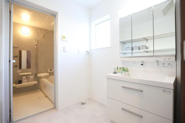 中鶴崎Ｗ　新築の独立洗面台|明るい窓から自然光が差し込む洗面所は清潔感のある白を基調とした空間です。三面鏡の収納スペースで日用品をすっきり整理しやすいです。隣接する浴室へのアクセスもスムーズで実用的なレイアウトです。