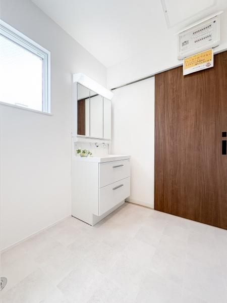 中鶴崎Ｗ　新築の独立洗面台|明るい窓から自然光が差し込む洗面所は清潔感のある白を基調とした空間です。三面鏡の収納スペースで日用品をすっきり整理しやすいです。隣接する浴室へのアクセスもスムーズで実用的なレイアウトです。