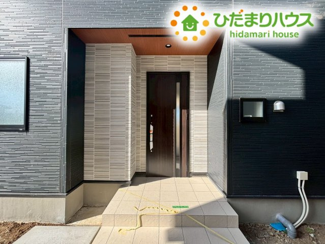 東松山市六軒町　新築一戸建て　ブルーミングガーデン　01のエントランス|木目調のドアが温かみを感じさせる玄関ポーチです！深い軒があるため、雨の日でも濡れずに鍵を開けられます。玄関周りはシンプルにまとめられ、季節の植栽や鉢植えを飾って、季節ごとの表情を楽しむこともできそう♪