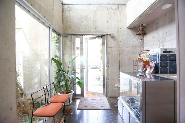 八幡店舗付中古の内装|コンクリート打ちっぱなしの壁面が印象的なエントランスです。大きなガラス窓から自然光が差し込み明るい空間が広がっています。観葉植物やベンチを設置することで清潔感があります。