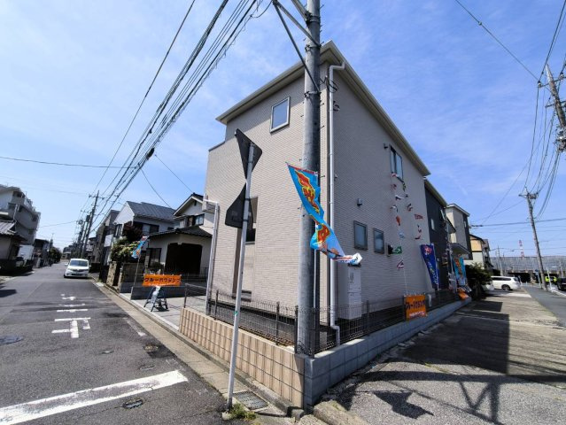 三郷市　早稲田5丁目　新築戸建　全2棟の前面道路含む現地写真|開放感のある角地に立地した新築戸建。2方向が道路に面しているため、圧迫感が少なく、風通しや採光にも期待できる住まいです。道路側から建物全体が見えやすく、明るいベージュ系の外観もすっきりとした印象。