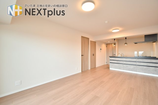 ソフィア上尾B棟の居間・リビング|リビング側からキッチンまで視線が抜ける一体空間で、家族の気配が感じられます。バルコニーに面した窓で換気もしやすく、在宅ワークや来客時にもレイアウトを変えて使い分け可能。床色も明るい印象です。