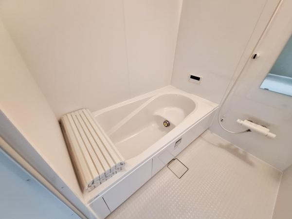 横塚2丁目1期1号棟の浴室|シンプルなデザインのバスルームです。浴槽にフタが備わっており使いやすさを感じられます。清潔感のあるカラーでまとめられています。床には滑りにくい素材が使用されています。