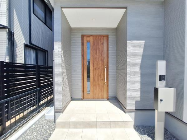横塚2丁目1期1号棟の玄関|明るい玄関アプローチが広がり木目調のドアがアクセントとなっています。スタイリッシュな外観と落ち着いた色味が特徴です。宅配ボックス付きで利便性も高いです。ゆとりあるスペースが魅力の玄関です。