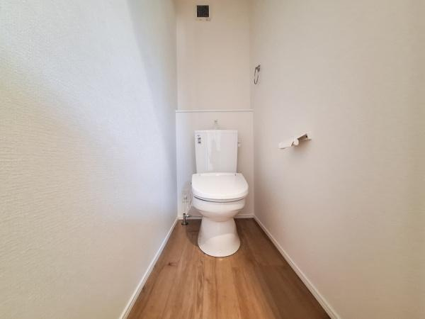 横塚2丁目1期2号棟のトイレ|シンプルなデザインのトイレです。床材との調和がとれた落ち着いた空間になっています。壁面も明るい色合いで開放感があります。換気用の設備も設置されています。手洗い付きのタンクが設けられています。