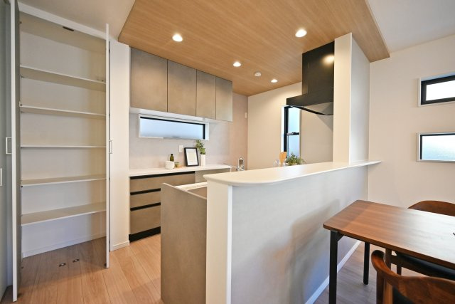 西宮市甲子園口5丁目新築一戸建て│4LDK+駐車1台可のキッチン|キッチン上部に折下天井を採用でデザイン性を向上させています。ダウンライトを採用し、作業性を確保。キッチン脇にはパントリー収納、可動棚収納庫が設けられています。