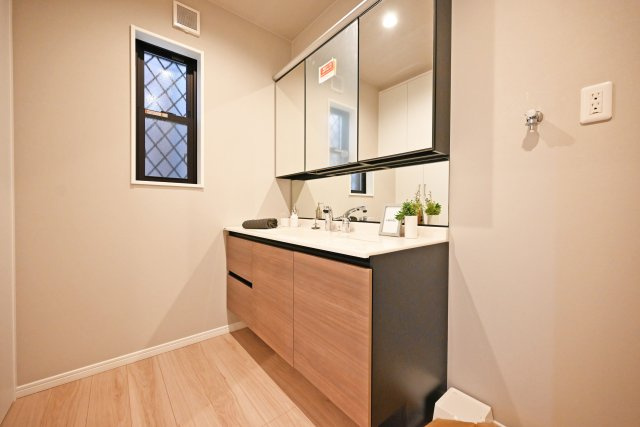 西宮市甲子園口5丁目新築一戸建て│4LDK+駐車1台可の洗面所|1階洗面室に入ってすぐの内観写真です。洗面台は3面鏡裏収納付きのドレッサーを採用しています。小窓も設けているため、電気乾燥機等によりこもる湿気もしっかり排出できます。