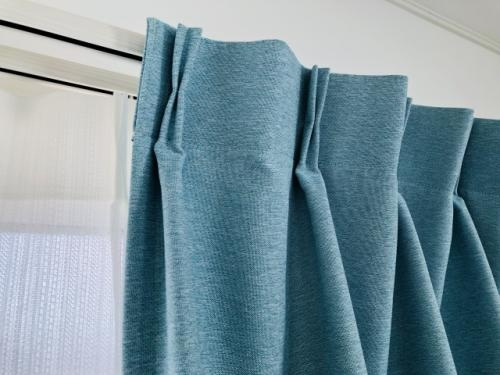 カーテンレールに青みがかったカーテンが掛けてある写真