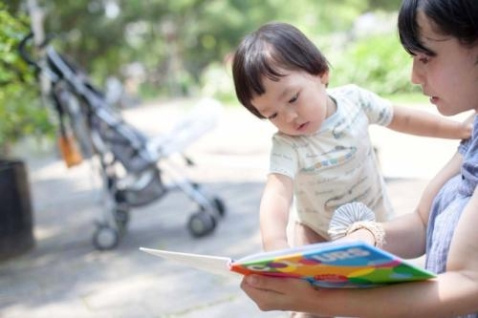 お母さんが公園で子どもに絵本を読み聞かせている写真