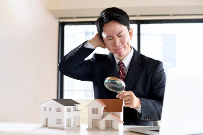 虫眼鏡で家の模型を観察する男性