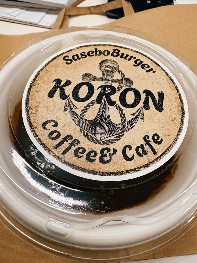 ２枚目：イカリのイラストと「Sasebo Burger KORON」のロゴステッカーが貼られたテイクアウト用カレー容器のフタのアップ写真