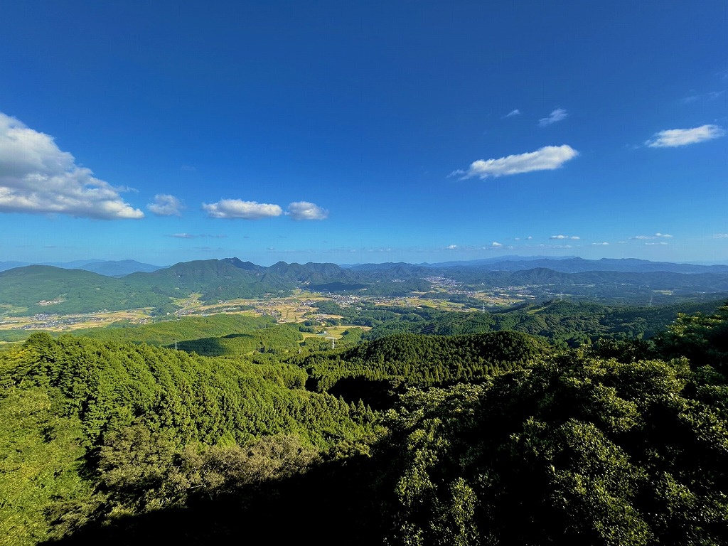 ３枚目：（山々の眺望）   快晴の青空のもと、どこまでも青々と広がる山並みと街並みを眼下に見渡す雄大な景観の写真